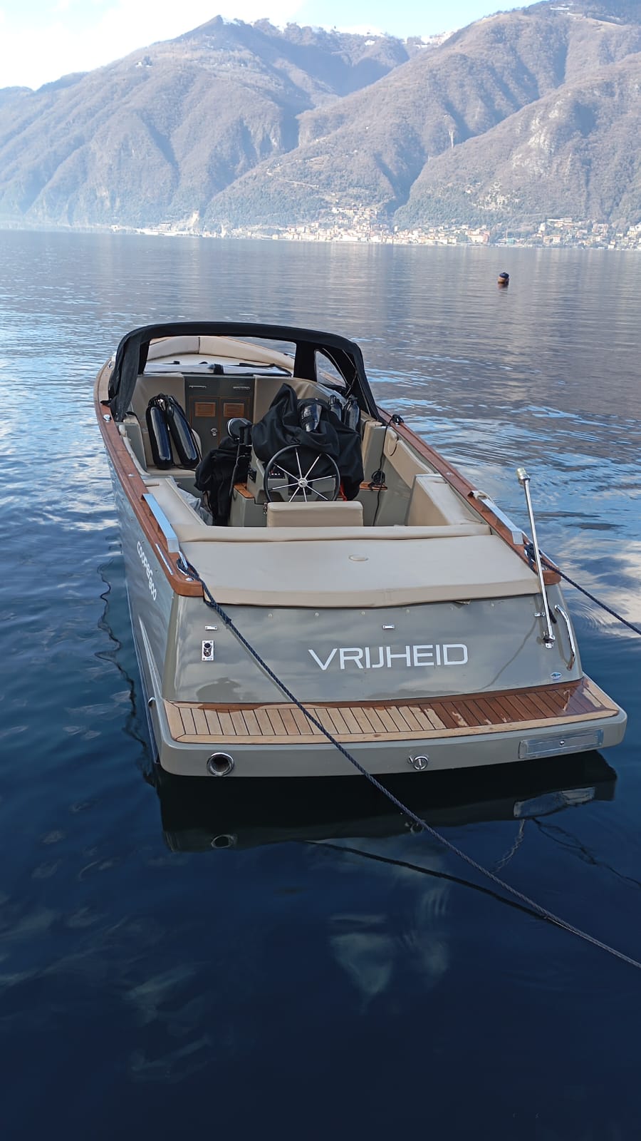 Real stern view of the Cooper 800 moored on Lake Como, with teak swim platform, wraparound cream seating, helm console and black bimini