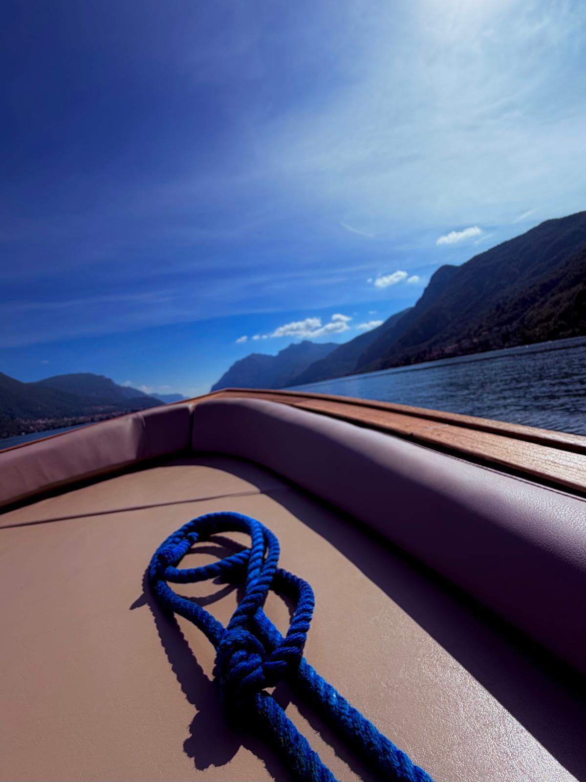The boat's bow and a coiled blue rope, looking out over Lake Como